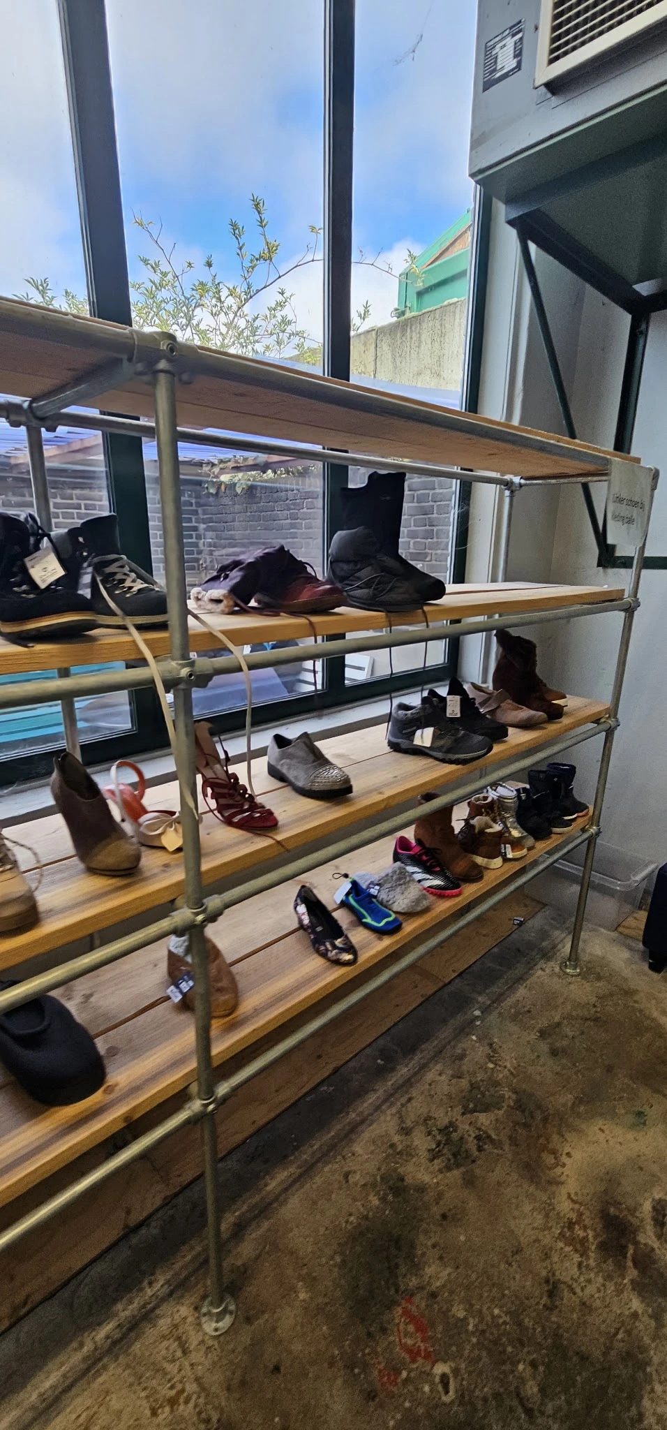 Metalen stellingkast met drie niveaus vol tweedehands schoenen en laarzen in verschillende kleuren en stijlen