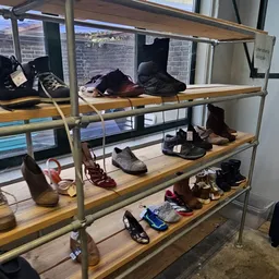 Metalen stellingkast met drie niveaus vol tweedehands schoenen en laarzen in verschillende kleuren en stijlen