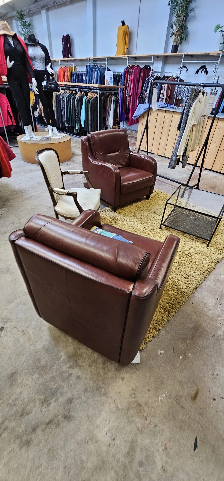 Bruinleren banken en stoelen uitgestald op gele vloerkleed in kringloopwinkel