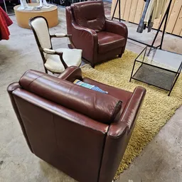 Bruinleren banken en stoelen uitgestald op gele vloerkleed in kringloopwinkel