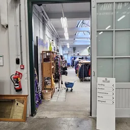 Winkelvloer met kledingrekken, stellingen en winkelwagen in kringloopwinkel
