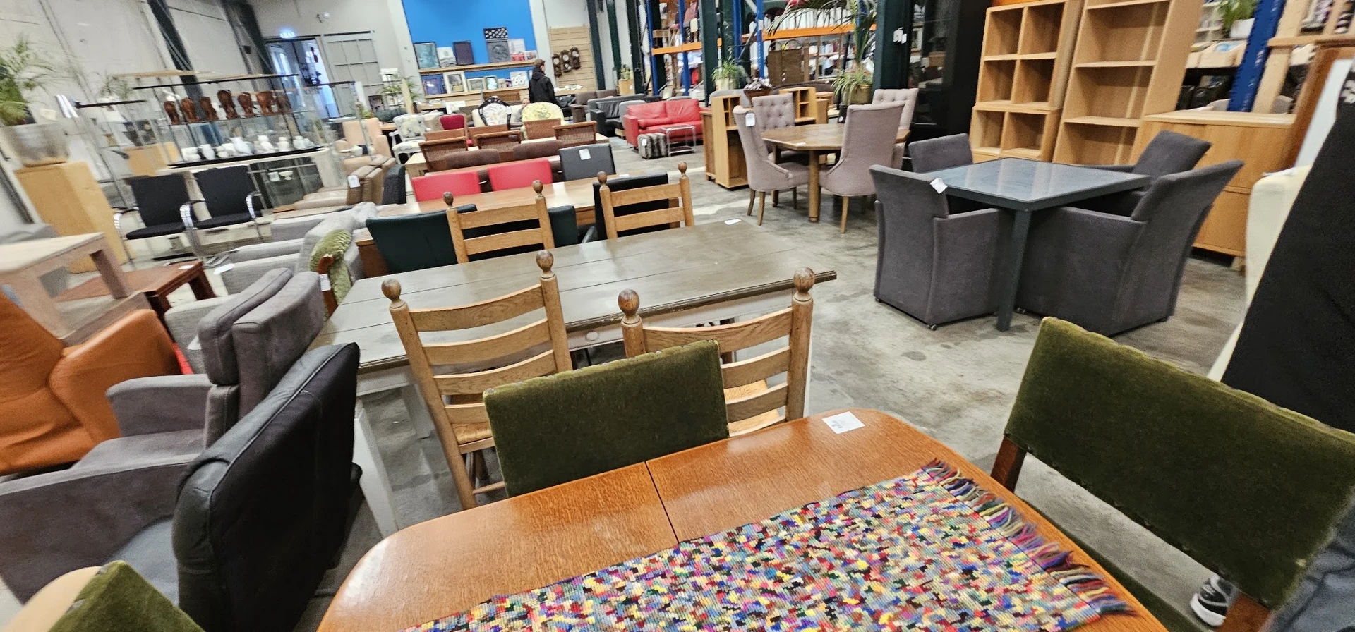 Winkelinterieur met houten stoelen met groene zitting, houten tafels en meubels, stellingen met dozen op de achtergrond