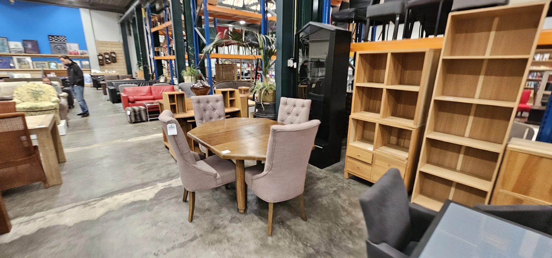 Houten eettafel met vier roze gestoffeerde stoelen en houten kasten in kringloopwinkel