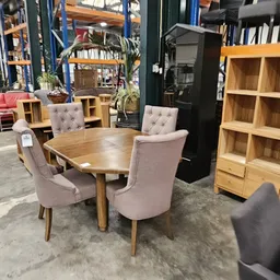 Houten eettafel met vier roze gestoffeerde stoelen en houten kasten in kringloopwinkel