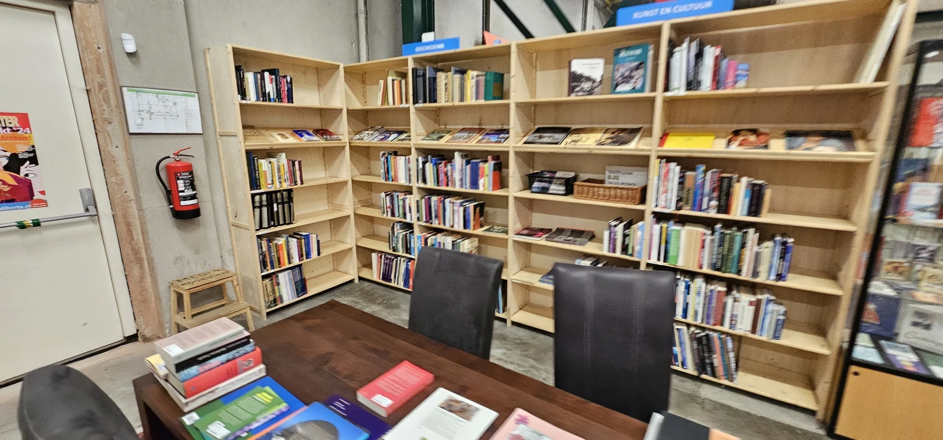 Houten boekenkasten vol met boeken en media in een winkel, met twee zwarte stoelen op de houten vloer.