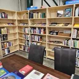 Houten boekenkasten vol met boeken en media in een winkel, met twee zwarte stoelen op de houten vloer.