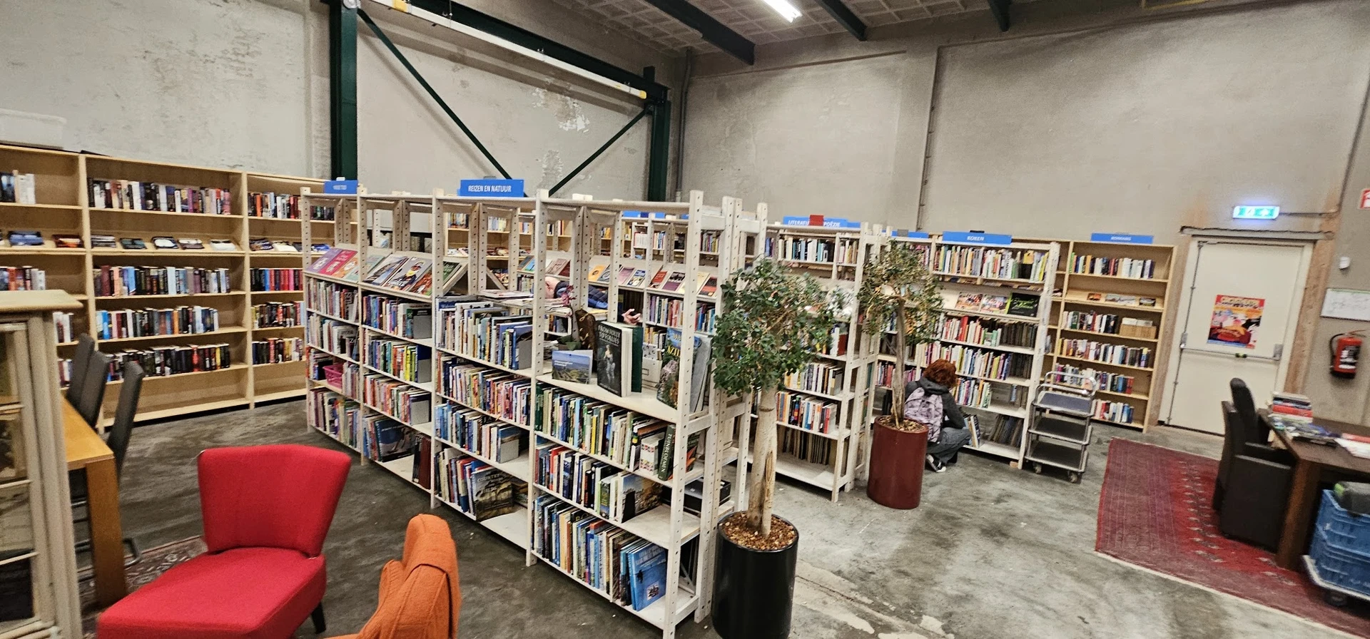 Boekenrekken met tweedehands boeken, rode stoelen en planten in een kringloopwinkel