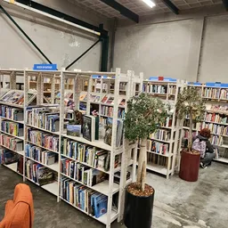 Boekenrekken met tweedehands boeken, rode stoelen en planten in een kringloopwinkel