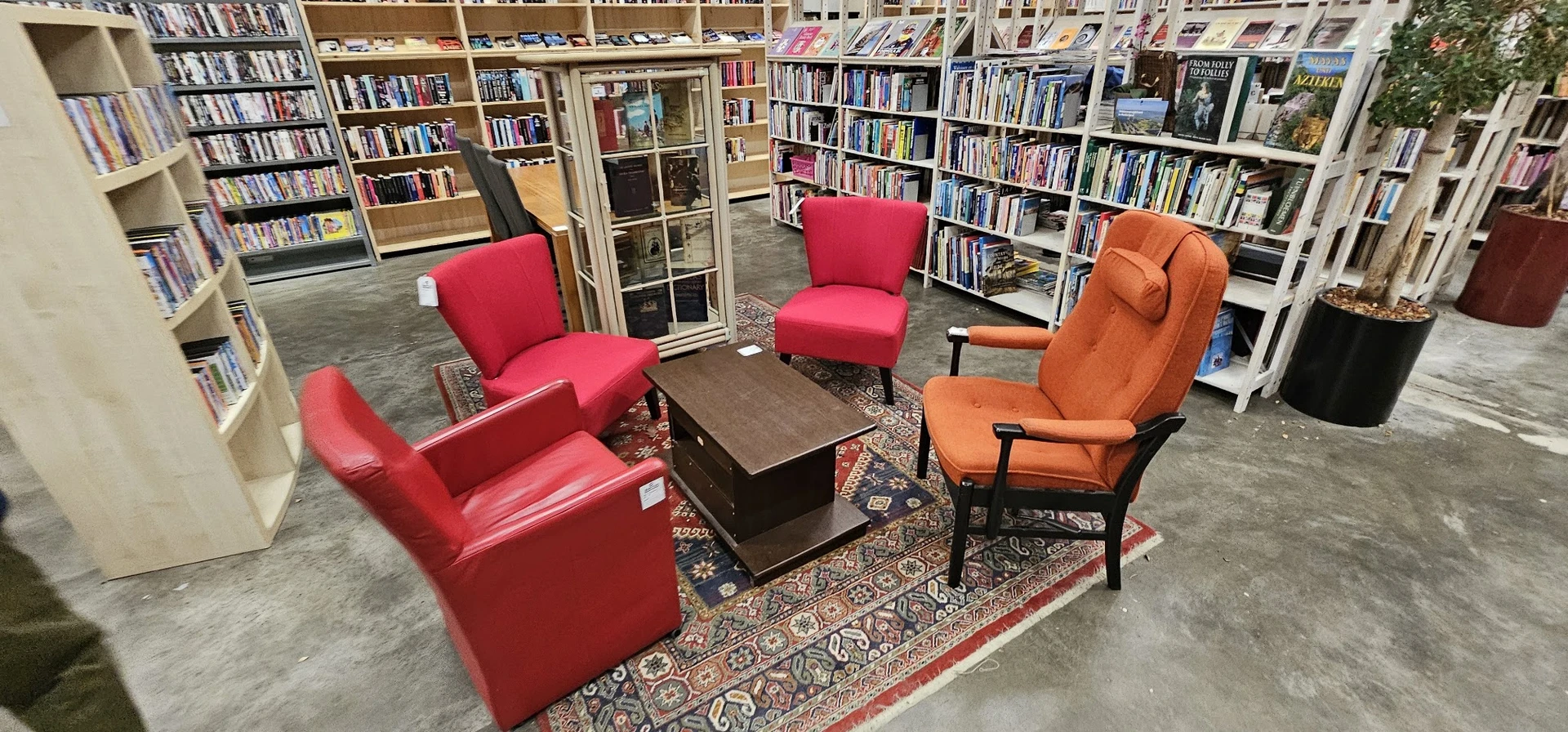 Zithoek met rode en oranje fauteuils rond een tafel, omgeven door boekenkasten in een kringloopwinkel