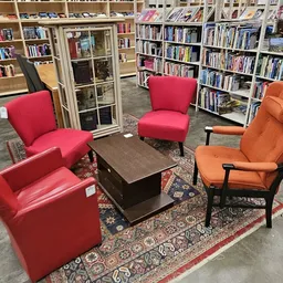 Zithoek met rode en oranje fauteuils rond een tafel, omgeven door boekenkasten in een kringloopwinkel