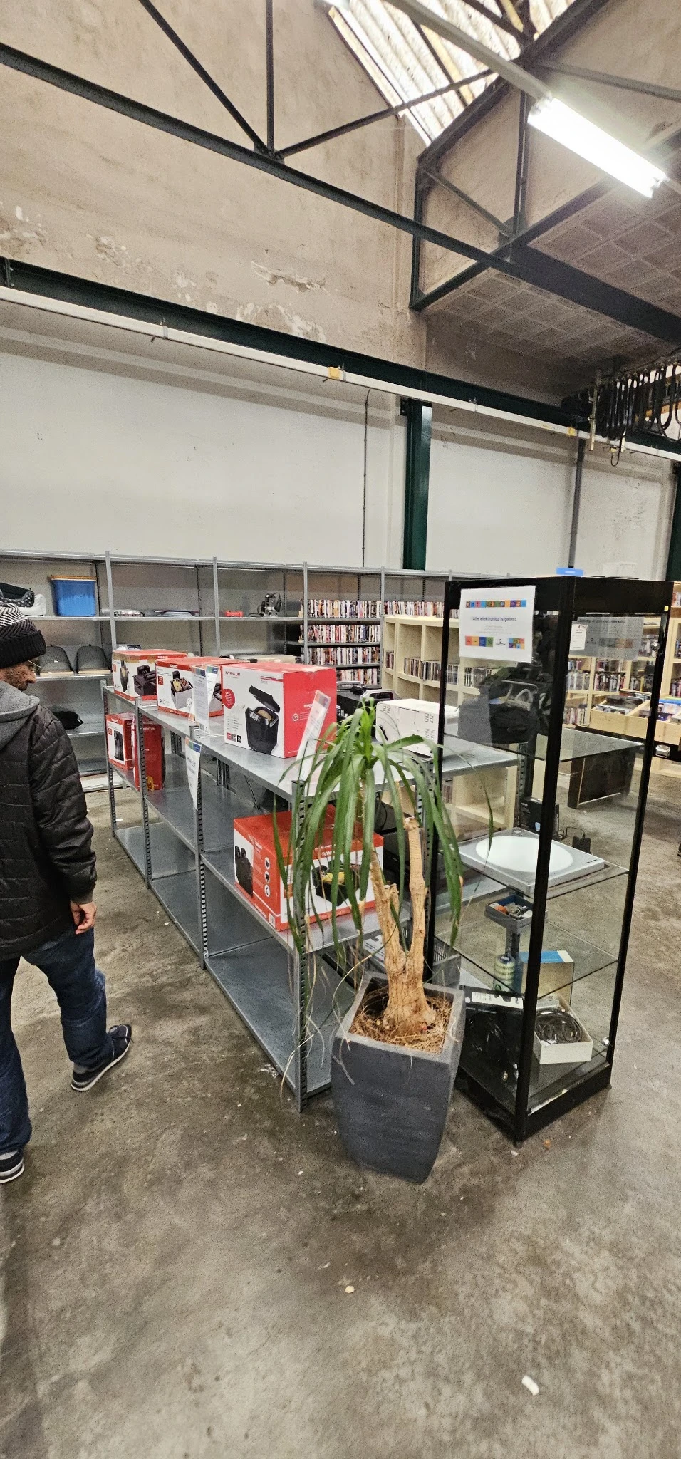Winkelrek met rode verpakte elektronicaartikelen, boeken en een plant ertegenaan