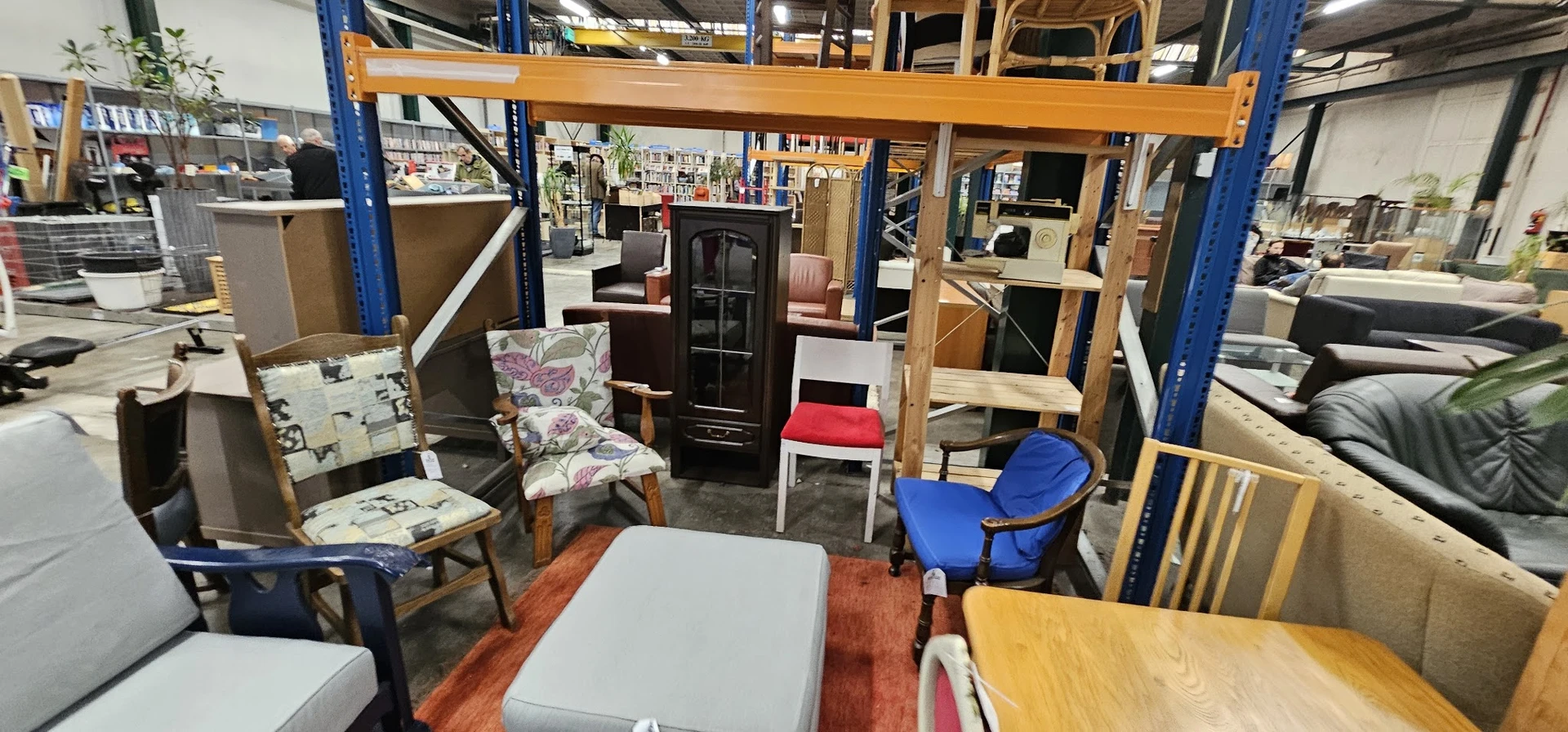 Winkelvloer met diverse meubels en huishoudspullen, inclusief stoelen, tafels en een kast tegen houten stellingen