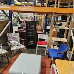 Winkelvloer met diverse meubels en huishoudspullen, inclusief stoelen, tafels en een kast tegen houten stellingen