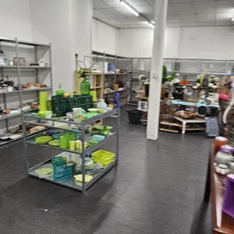 Winkelvloer van kringloopwinkel met diverse stellingen vol spullen, grijs beton, witte muren en kolommen