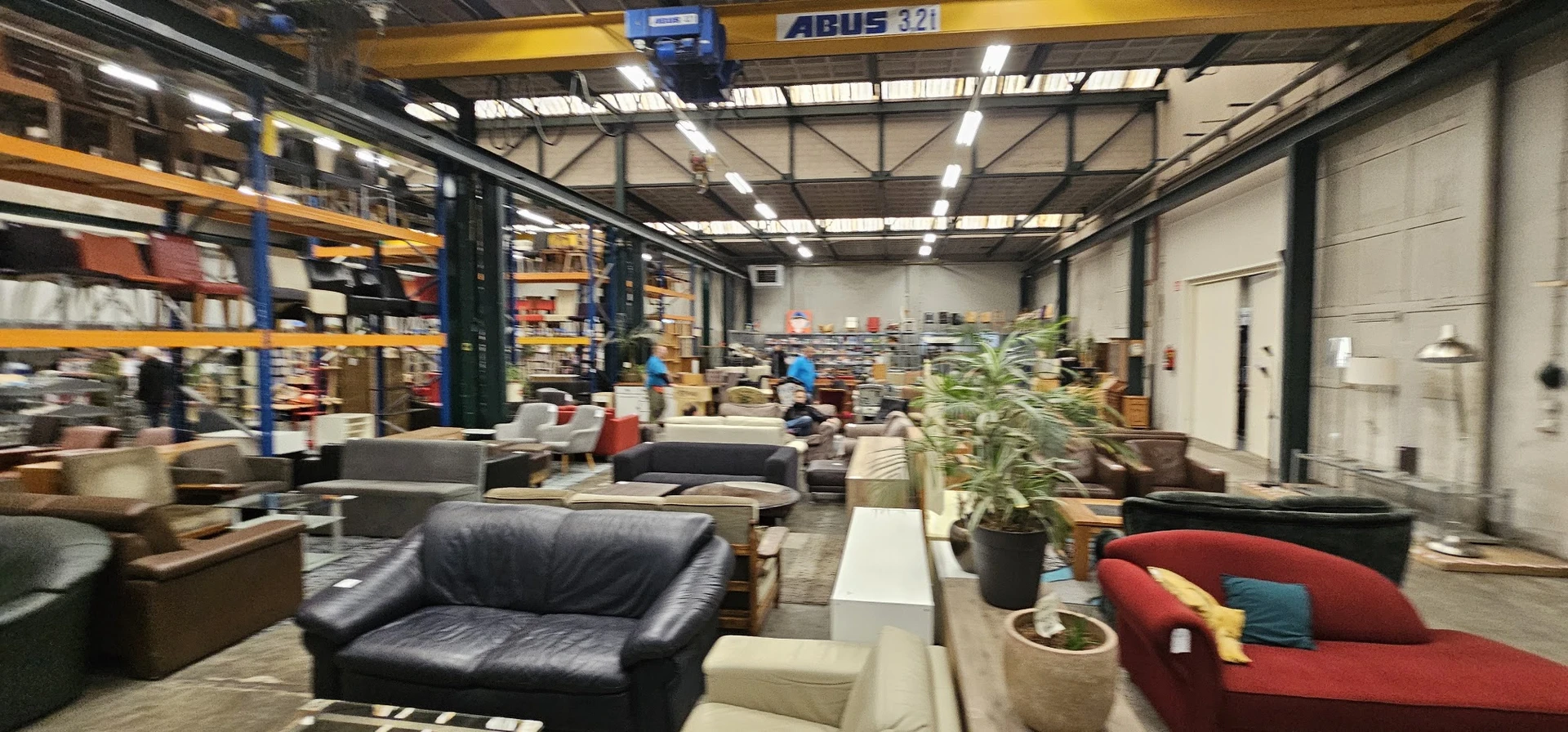 Winkelvloer met zitmeubels en meubels, stellingen op de achtergrond, industrieel plafond met overhead-kraan