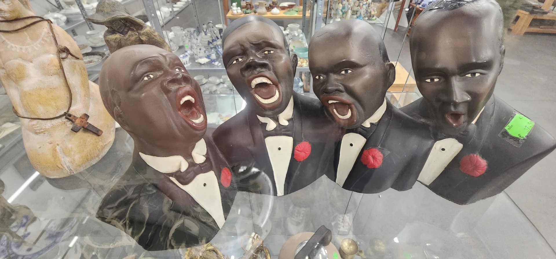 Vier zwarte decoratieve busten in formele kleding, uitgestald in een glazen vitrine in de winkel