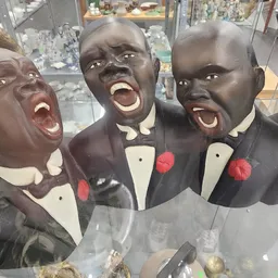 Vier zwarte decoratieve busten in formele kleding, uitgestald in een glazen vitrine in de winkel