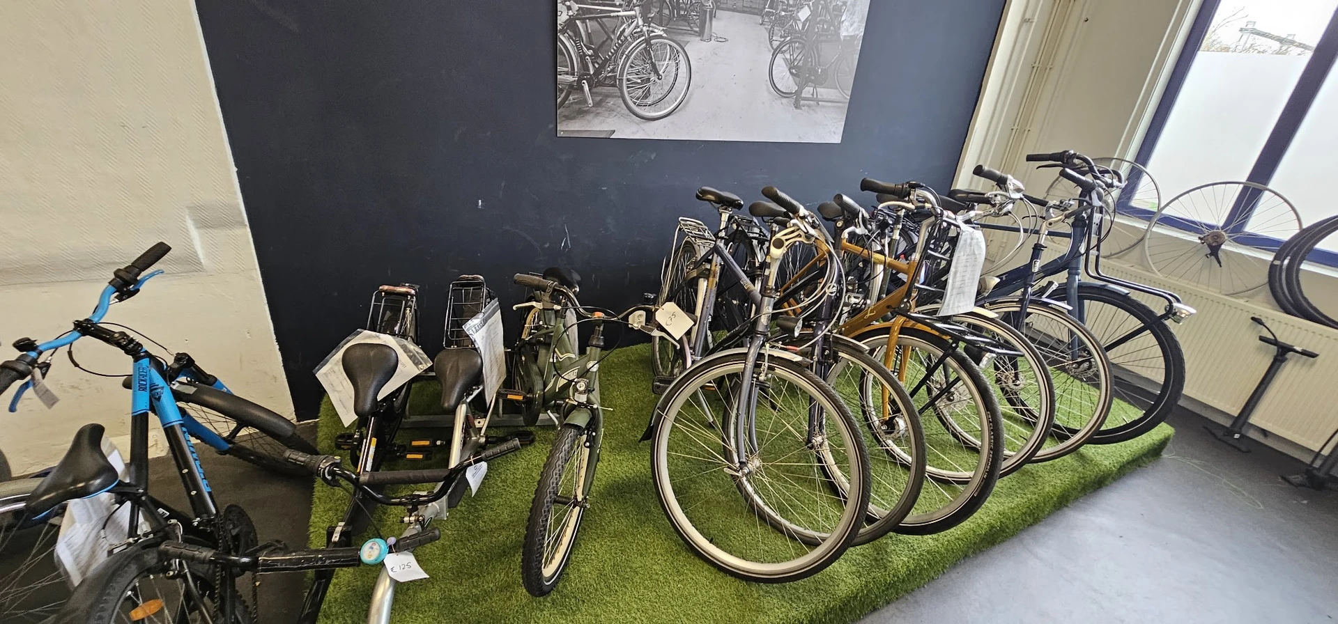 Uitgestalde tweedehandsfiets en andere fietsen op kunstgras in de kringloopwinkel
