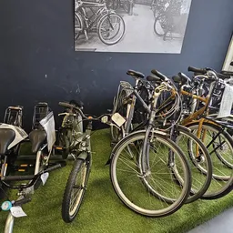 Uitgestalde tweedehandsfiets en andere fietsen op kunstgras in de kringloopwinkel