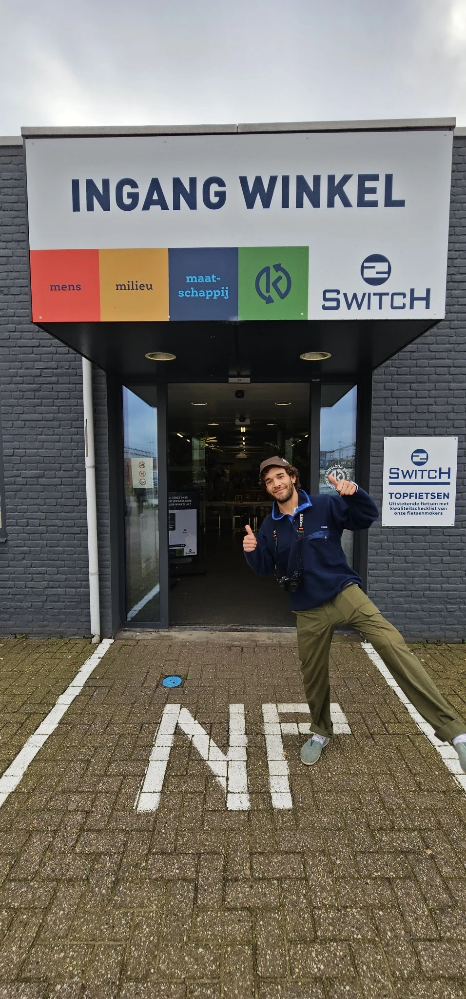 Ingang van 2Switch kringloopwinkel met medewerker die naar camera wijst