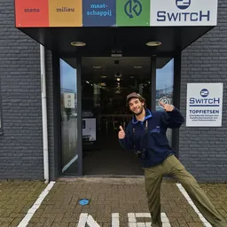 Ingang van 2Switch kringloopwinkel met medewerker die naar camera wijst