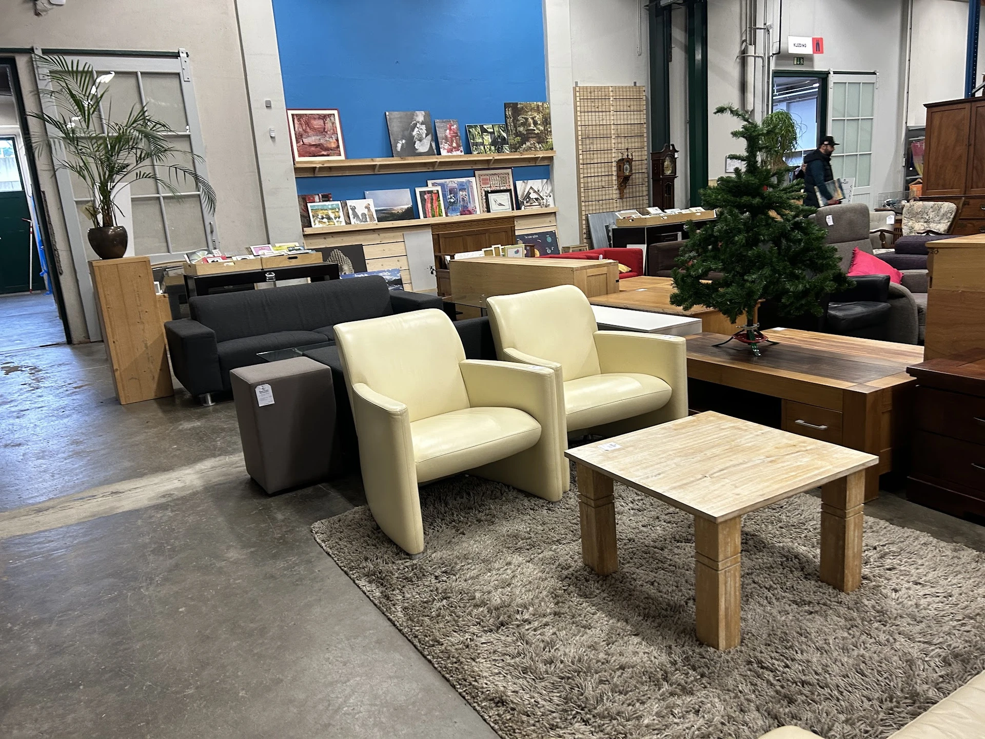 Winkelvloer met meubels: twee crèmekleurige fauteuils, zwarte poef, houten salontafel op vloerkleed, en diverse meubels op de