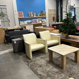 Winkelvloer met meubels: twee crèmekleurige fauteuils, zwarte poef, houten salontafel op vloerkleed, en diverse meubels op de