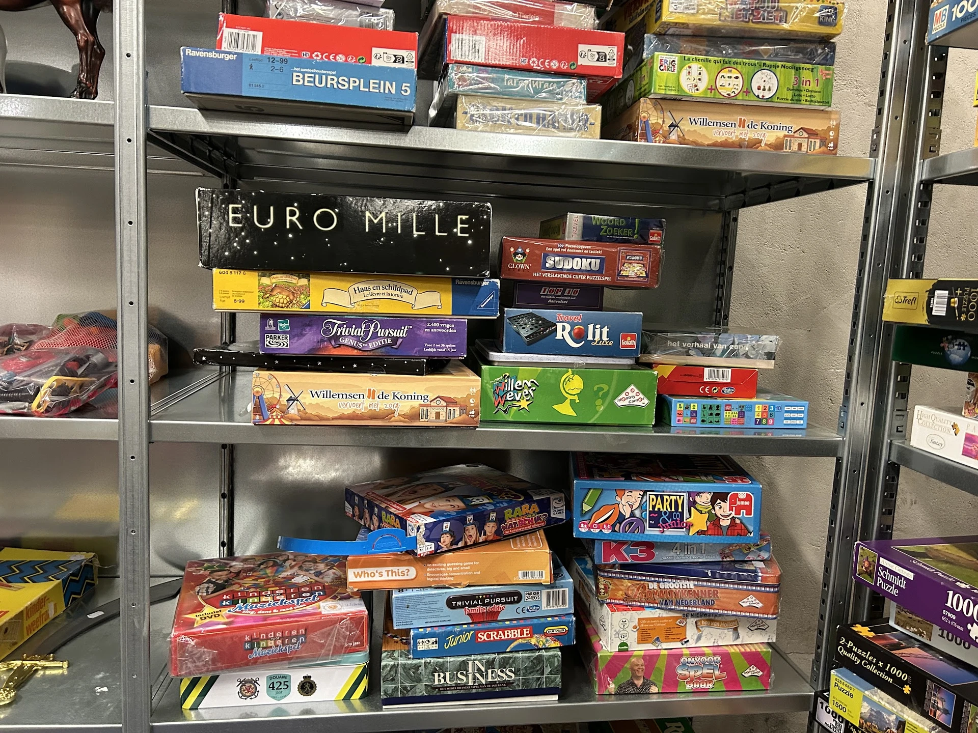 Stellingkast met uitgestalde gezelschapsspellen en bordspellen, waaronder Euromille, Trivial Pursuit en andere titels