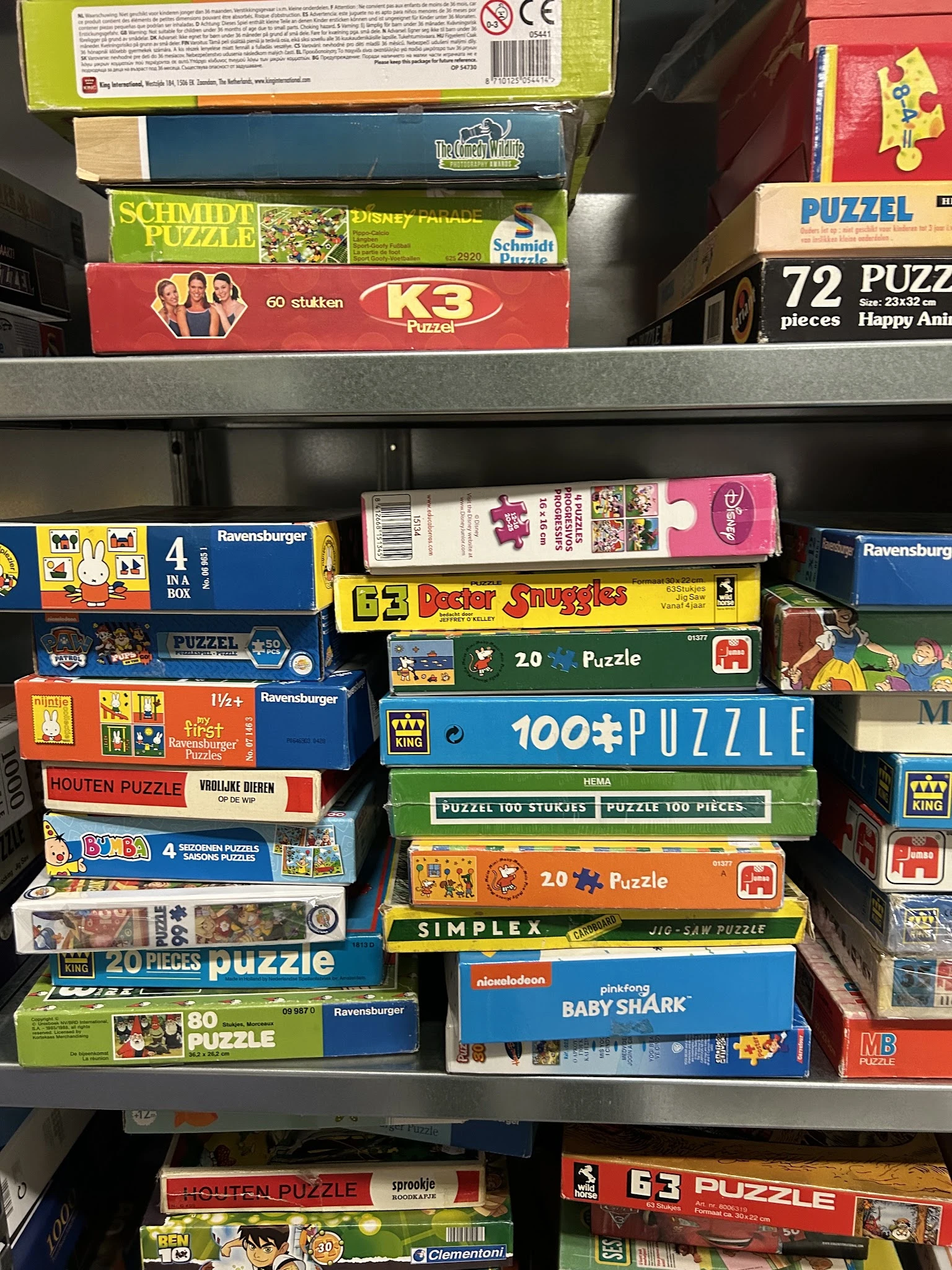 Stellingkast met stapels puzzelboxen en bordspellen, waaronder Ravensburger en ander speelgoed