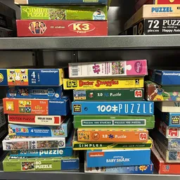 Stellingkast met stapels puzzelboxen en bordspellen, waaronder Ravensburger en ander speelgoed