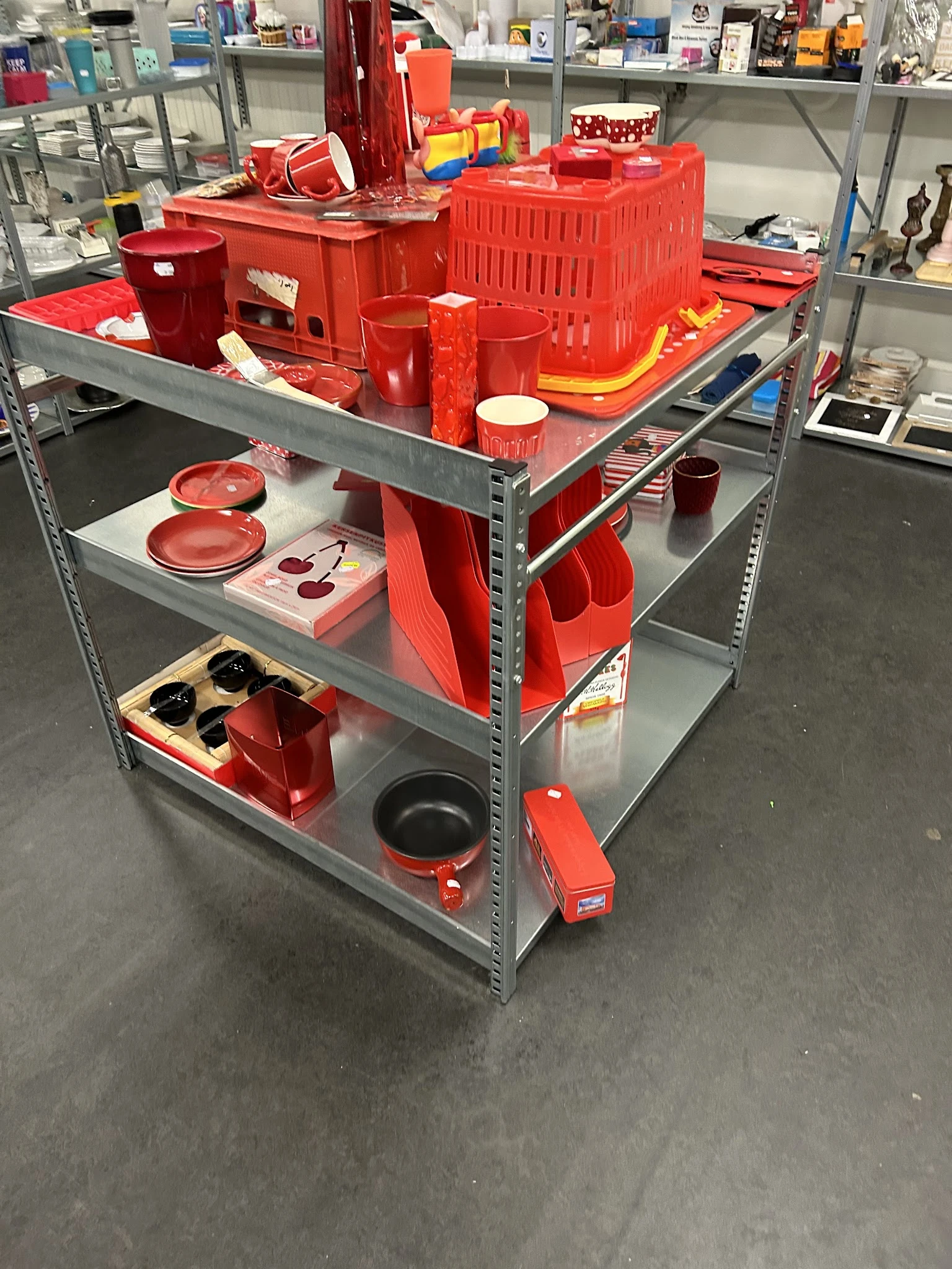 Stellingkast met rood serviesgoed en keukengerei, waaronder borden, pannen en rode plastic bakken