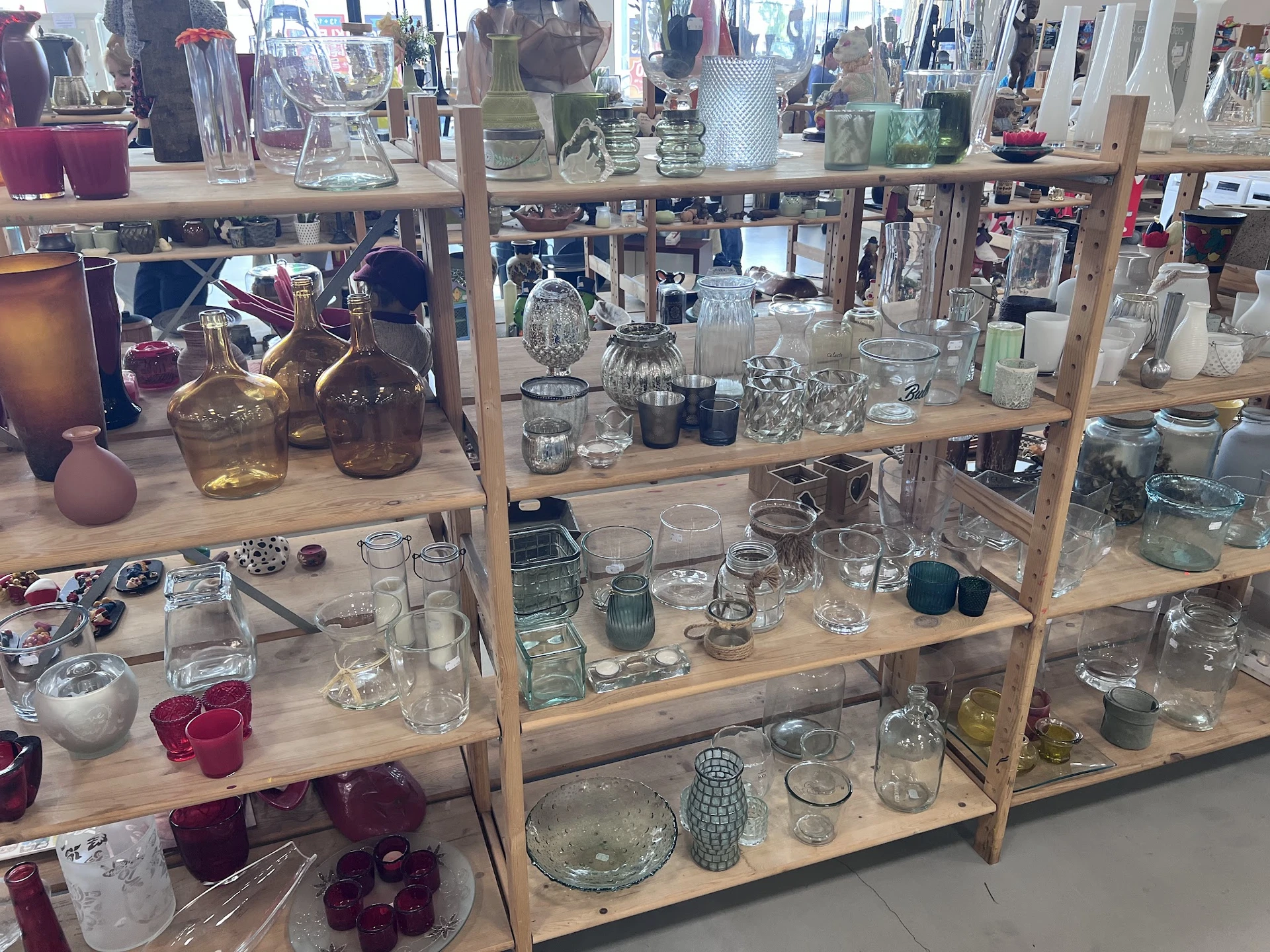 Houten stellingen met uitgestalde glazen vazen, kandelaars, kaarsen en decoratieve huishoudartikelen