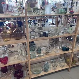 Houten stellingen met uitgestalde glazen vazen, kandelaars, kaarsen en decoratieve huishoudartikelen