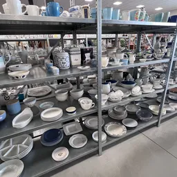 Vitrinekasten met uitgestald serviesgoed, borden, kopjes en huishoudelijke artikelen in verschillende maten en kleuren