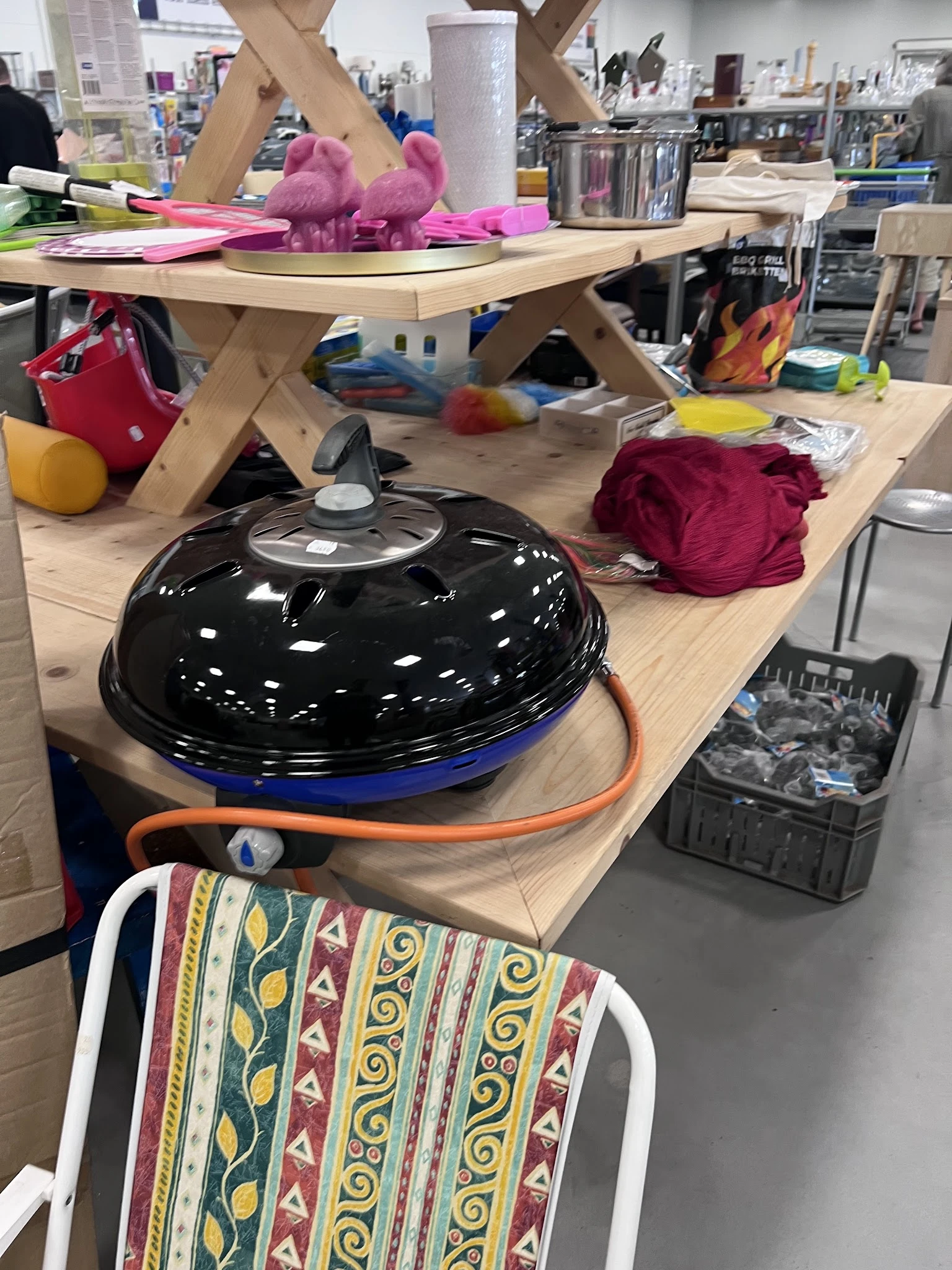 Tafel met diverse tweedehands artikelen waaronder een zwarte barbecuegrill, kleding en huishoudspullen