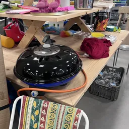 Tafel met diverse tweedehands artikelen waaronder een zwarte barbecuegrill, kleding en huishoudspullen