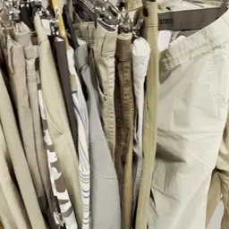 Rekken met tweedehands broeken en pantalons in beige, wit en taupe tinten