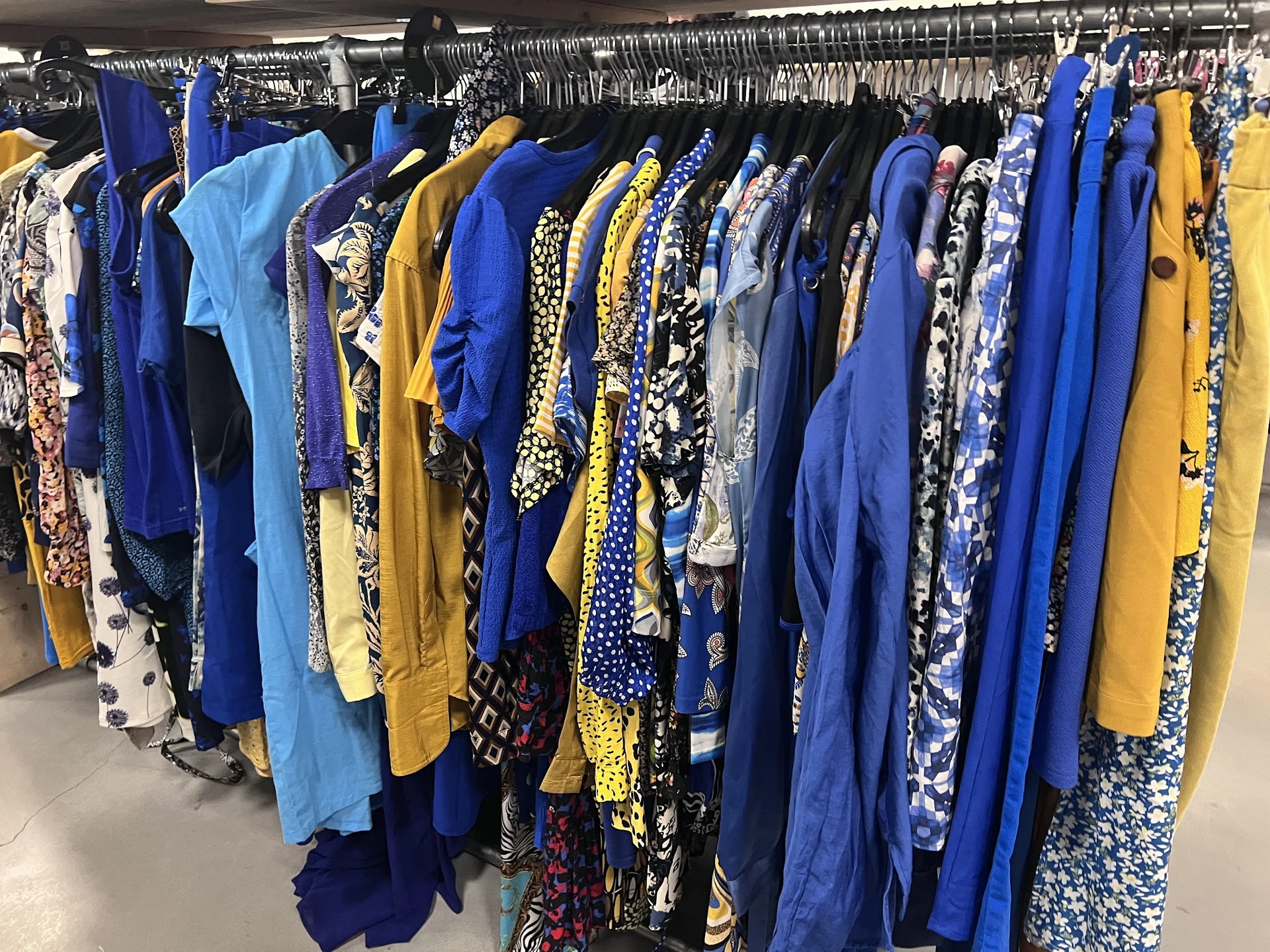 Rekken met tweedehands dameskleding in blauwe, gele en zwarte tinten