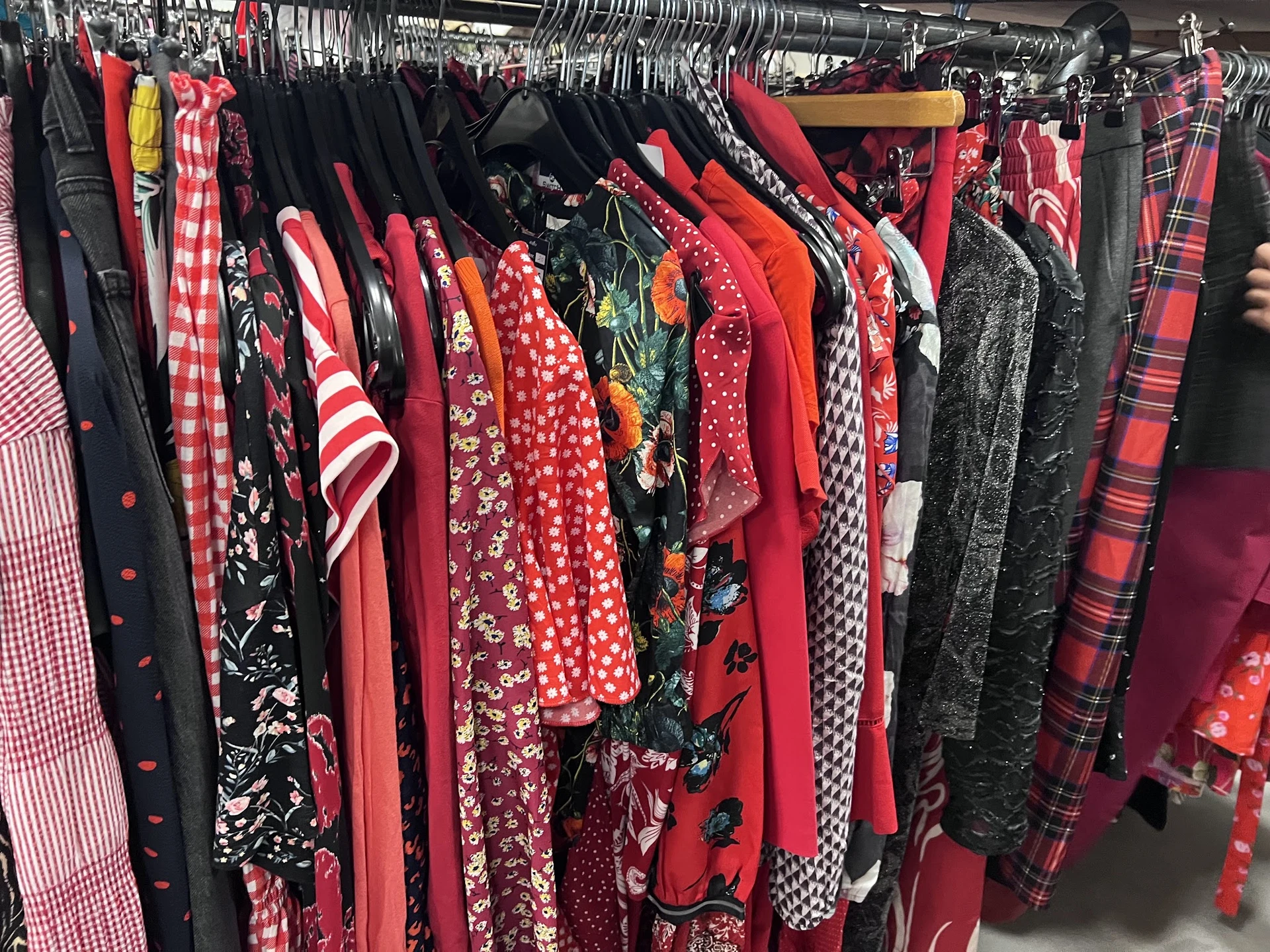Rekken met tweedehands dameskleding in verschillende kleuren en patronen, vooral rood, zwart en geruit