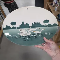 Decoratief bord met uitgestanst design van zwanen op water met bomen op de achtergrond