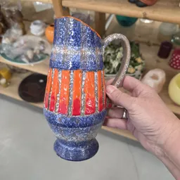 Close-up van een decoratieve kruik met blauw en oranje glazuur, gehouden in een hand
