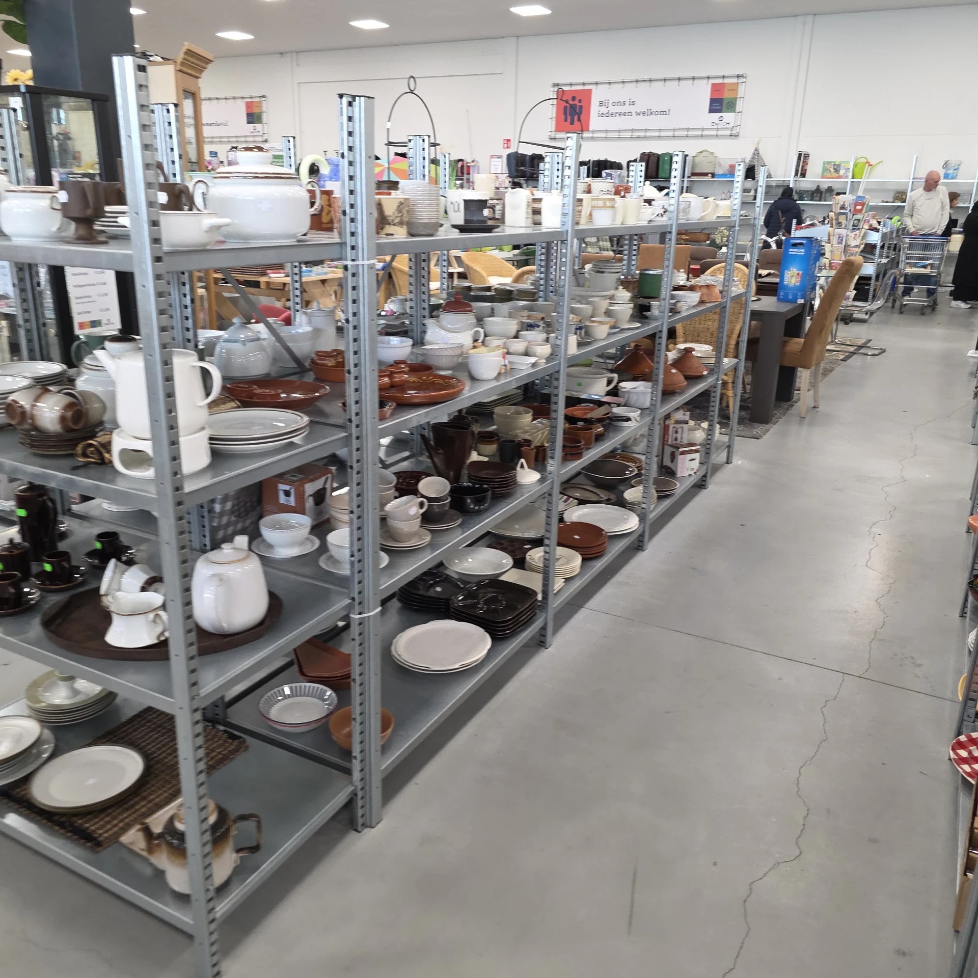 Metalen stellingen vol met serviesgoed, pannen, schalen en ander keukengerei in de kringloopwinkel