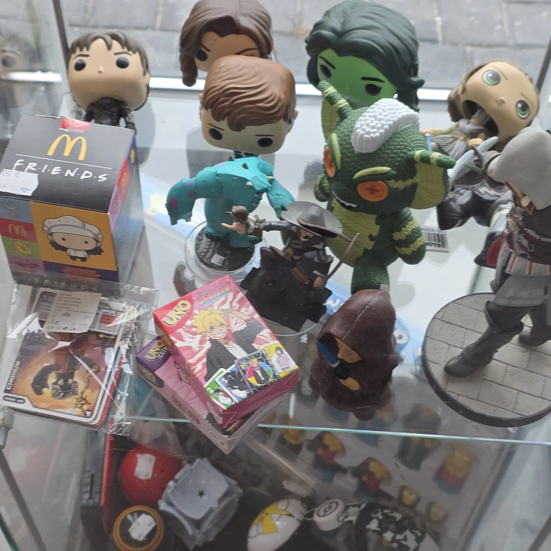 Verzameling speelgoed en collectibles op een glasplaat, inclusief Funko Pop-figuren, een groen monster en diverse actiefigure