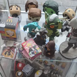 Verzameling speelgoed en collectibles op een glasplaat, inclusief Funko Pop-figuren, een groen monster en diverse actiefigure