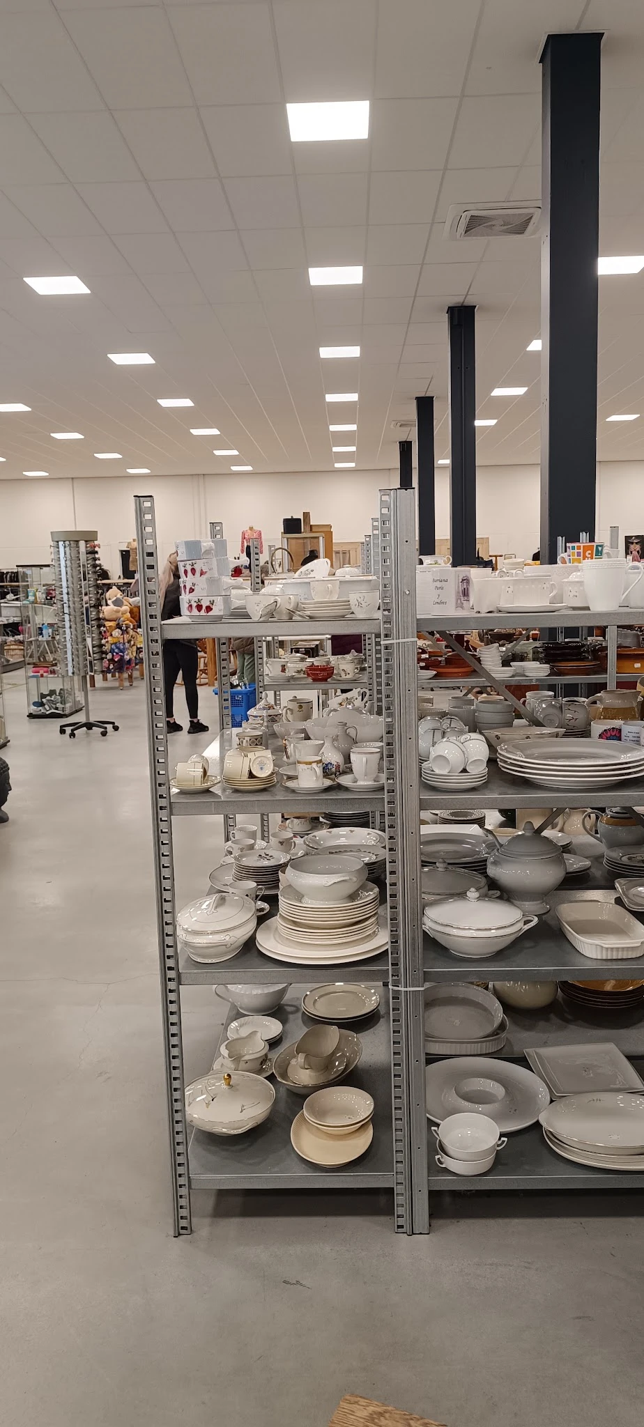 Metalen stellingen volgestapeld met wit en grijs serviesgoed, borden, schalen en kopjes in een kringloopwinkel