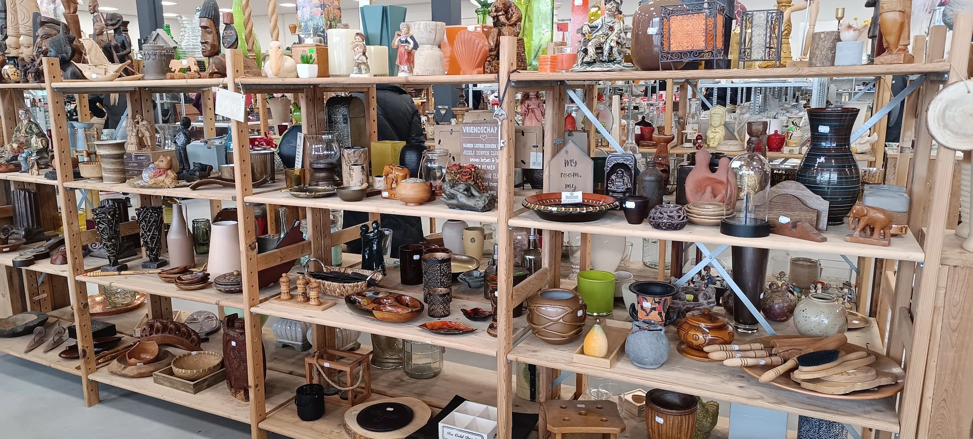Houten stellingen volgesteld met huishoudwaren, decoratie en diverse tweedehands artikelen in een kringloopwinkel