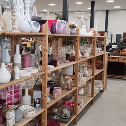 Houten stellingen volgestapeld met huishoudelijke artikelen, decoratie en serviesgoed in diverse kleuren en stijlen