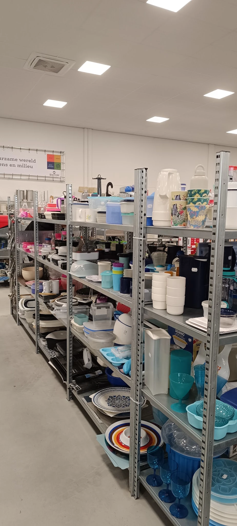 Metalen stellingen met diverse huishoudelijke artikelen, opbergdozen en keukengerei in de kringloopwinkel
