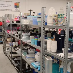 Metalen stellingen met diverse huishoudelijke artikelen, opbergdozen en keukengerei in de kringloopwinkel
