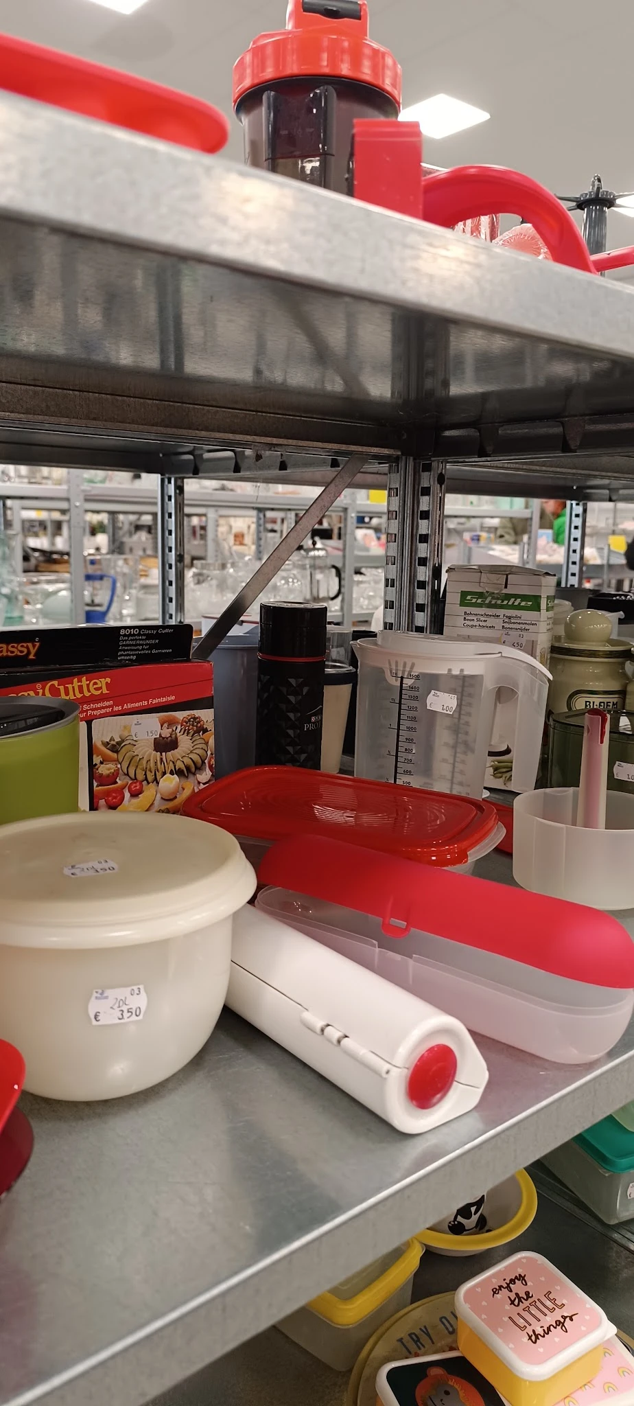 Diverse keukengerei en huishoudartikelen op een werktafel, waaronder rode schalen, een mixer, een snijder en andere gebruiksv